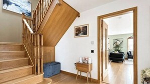 Uma escada de madeira leva a uma sala de estar com um banquinho azul, uma pequena mesa lateral de madeira e um quadro na parede.