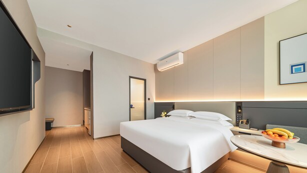 A modern hotel room with a bed, bedside table, and a small round table with fruit.