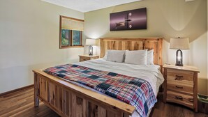 A bedroom with a wooden bed, a nightstand with a lamp, a wall-mounted TV, and a painting. - Lakefront 4BR/3.5BA retreat with beautiful views (Oakland)