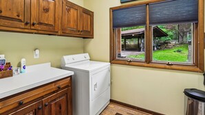 A kitchen with wooden cabinets, a white washing machine, and a window with a view of a garden. - Lakefront 4BR/3.5BA retreat with beautiful views (Oakland)