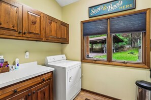 A kitchen with wooden cabinets, a white washing machine, and a window with a view of a garden. - Lakefront 4BR/3.5BA retreat with beautiful views (Oakland)