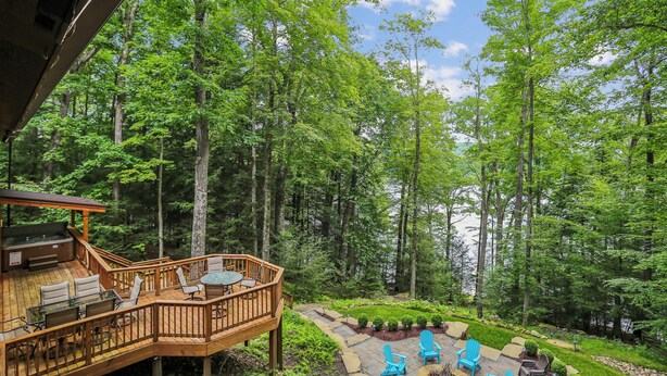 A wooden deck with outdoor seating, surrounded by a forested area with tall trees. - Lakefront 4BR/3.5BA retreat with beautiful views (Oakland)