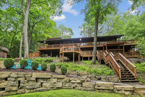 A multi-level wooden cabin with a stone retaining wall and a staircase leading to the upper levels. - Lakefront 4BR/3.5BA retreat with beautiful views (Oakland)