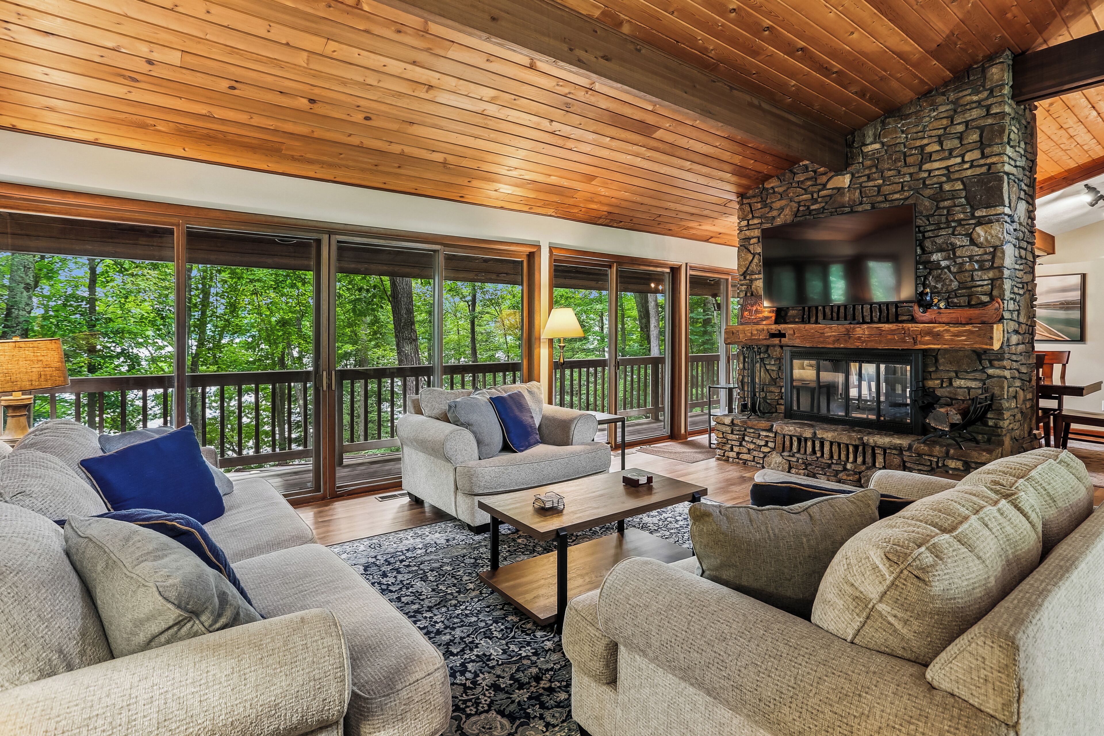 A spacious living room with a stone fireplace, large windows, and a cozy seating area.