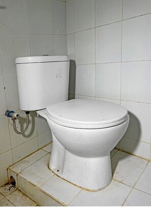 Eine weiße Toilette mit Tank und Sitz, vor einer gefliesten Wand platziert.