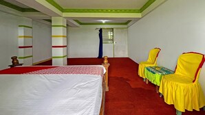 Quarto de hotel com uma cama, duas cadeiras, uma mesa e uma porta.