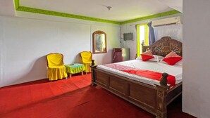 Quarto com cama de madeira, duas cadeiras amarelas, uma mesinha e um espelho.