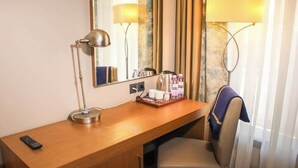 Een hotelkamer met een houten bureau, een stoel, een lamp, een spiegel en een raam met gordijnen.