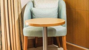 Een hoekkamer met een lichtblauwe fauteuil, een klein rond tafeltje, een houten deur en een gordijn.