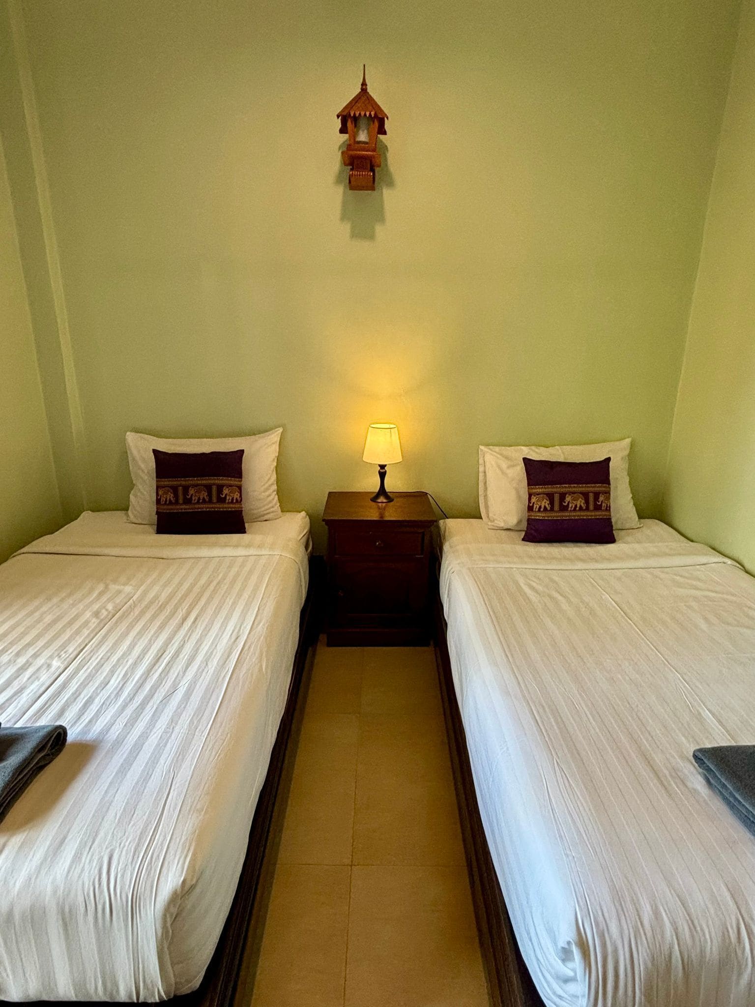 A hotel room with two beds, a nightstand with a lamp, and a wall-mounted light fixture.
