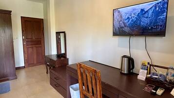 A room with a wooden desk, a television mounted on the wall, a wooden chair, a door, and a white trash bin.