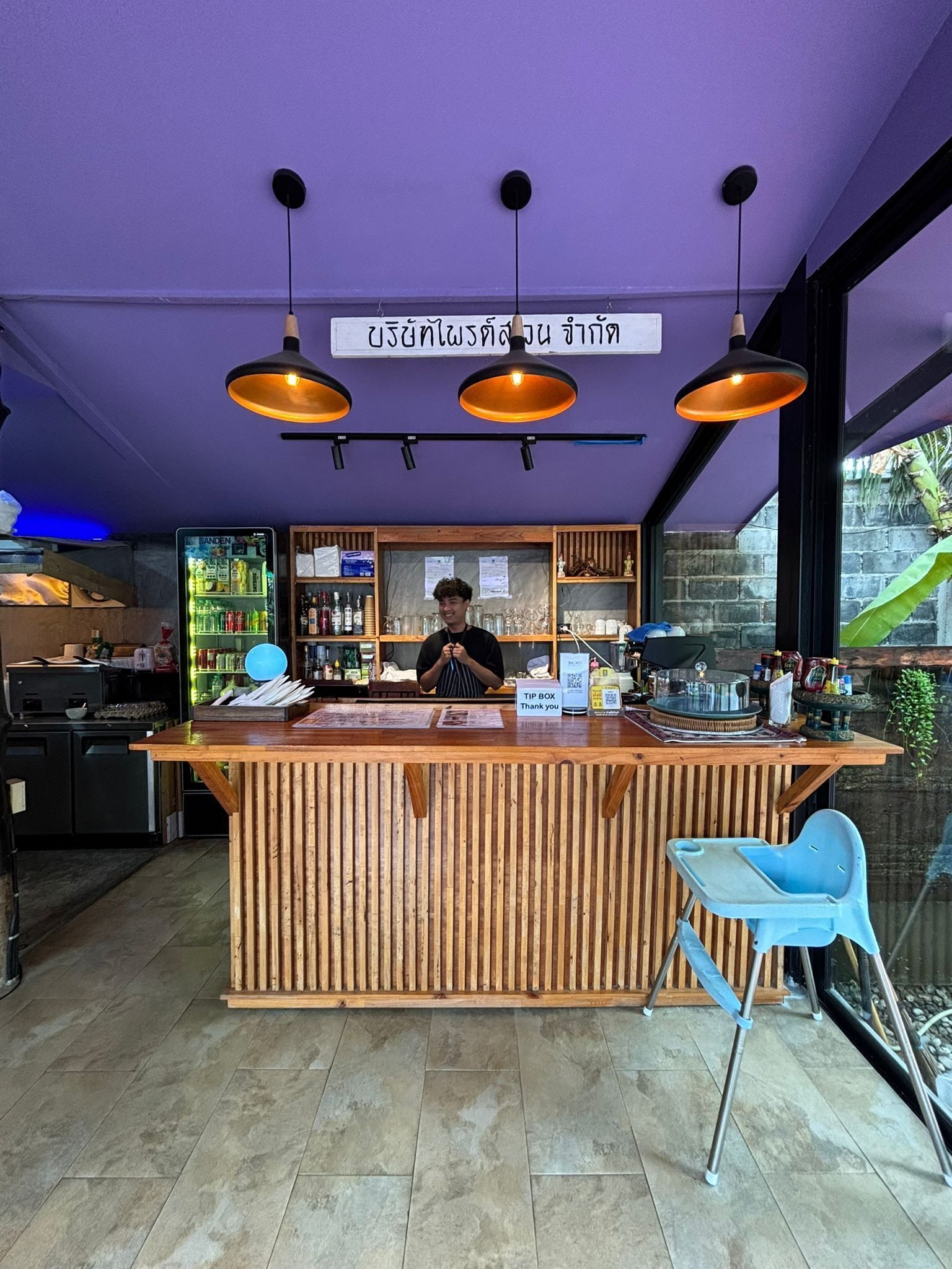 Un bar con mostrador de madera, luces colgantes y un letrero en un idioma extranjero.