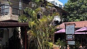 En byggnad med en balkong, en skylt för ett boutiquehotell och en skylt för thailändsk mat och kaffe.