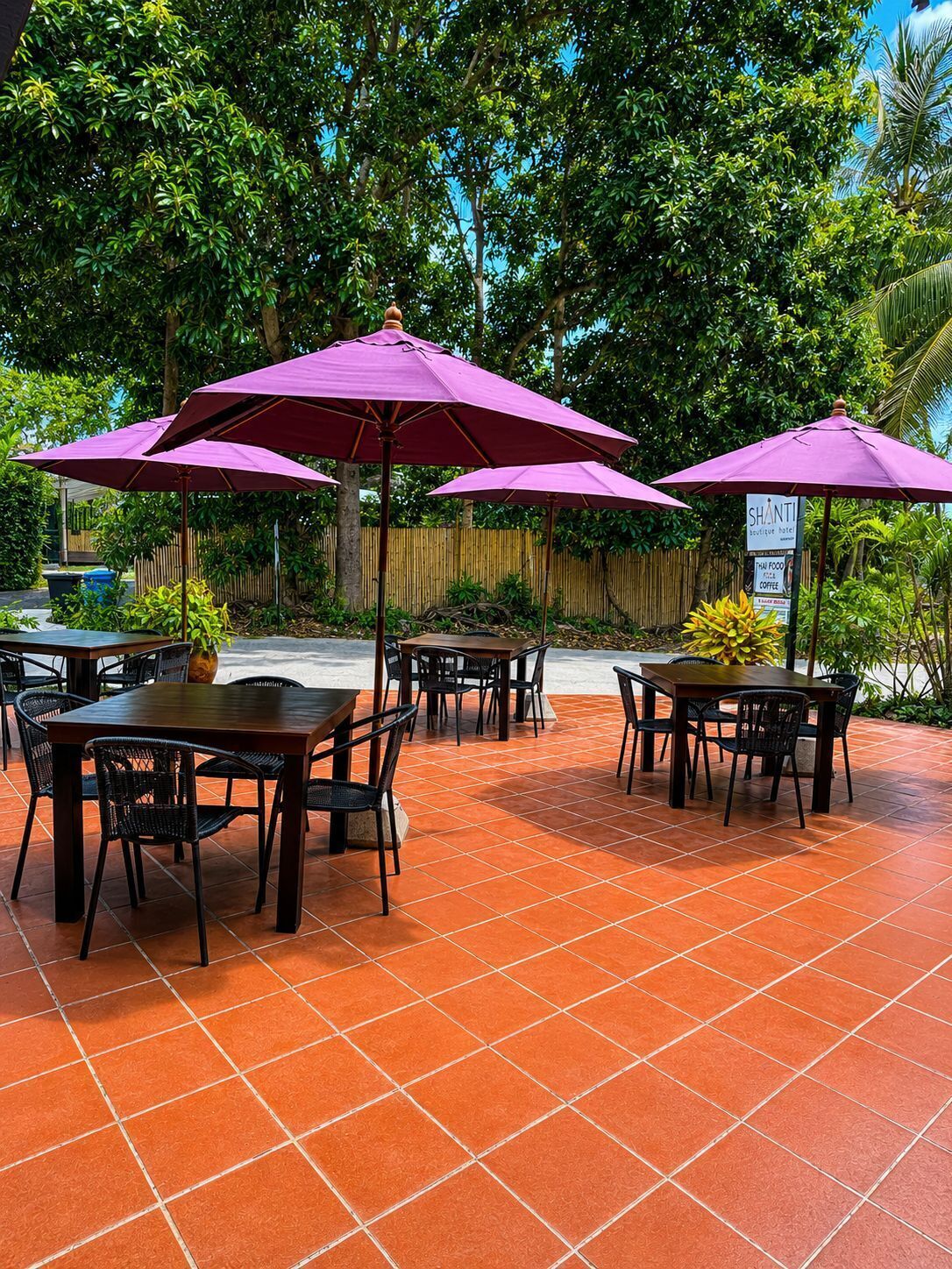 Eine Terrasse im Freien mit Tischen und Stühlen, umgeben von üppiger Bepflanzung und einem Bambuszaun.