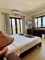 A hotel room with a bed, a desk, a television, and a view of the outdoors.