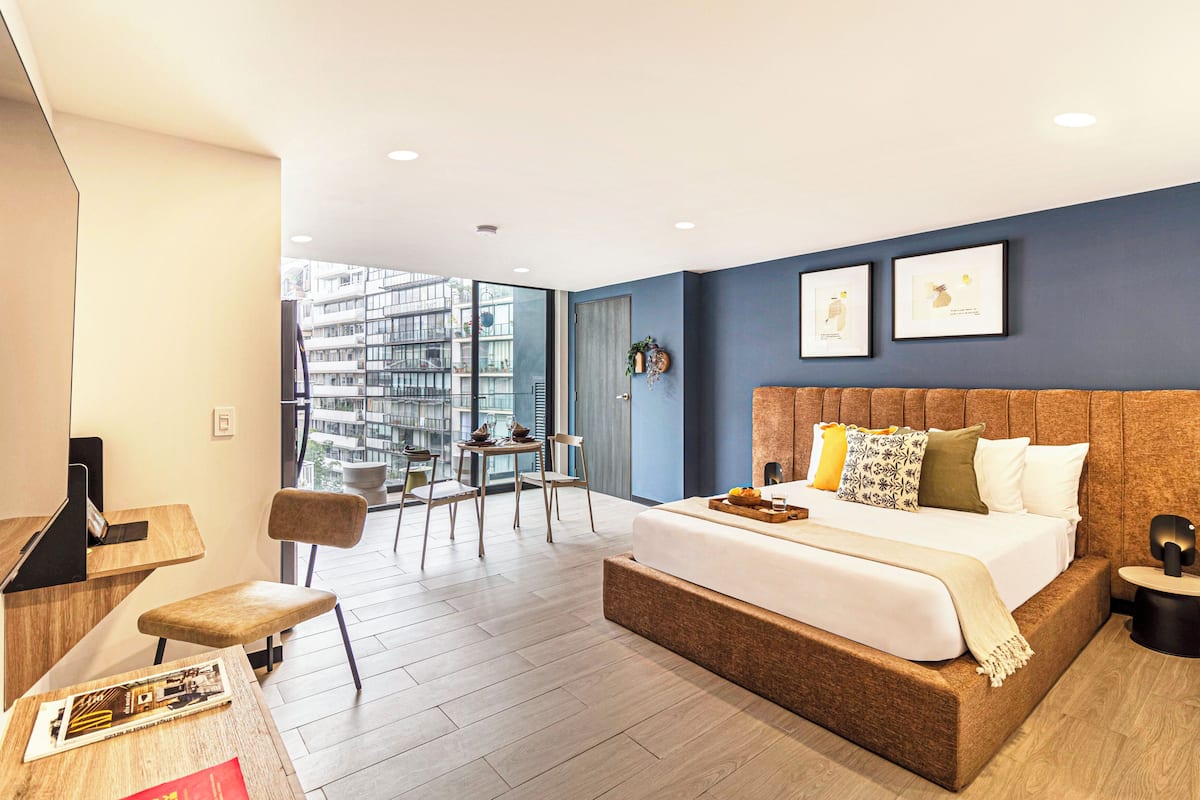 A modern hotel room with a large bed, a desk, and a balcony with a city view.