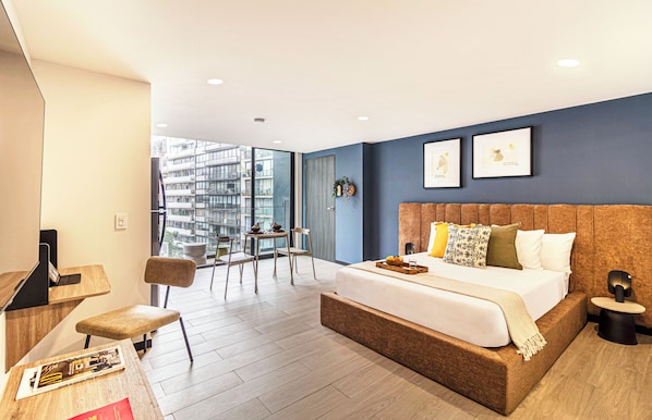Ein modernes Hotelzimmer mit einem großen Bett, einem Schreibtisch und einem Balkon mit Blick auf die Stadt.