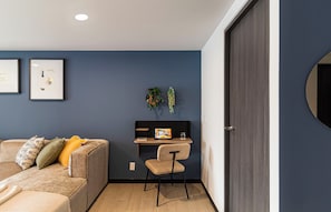 A modern room with a dark blue wall, a sofa with cushions, a small desk with a laptop, and a door. - Casa Sócrates By Kukun (Mexico City)