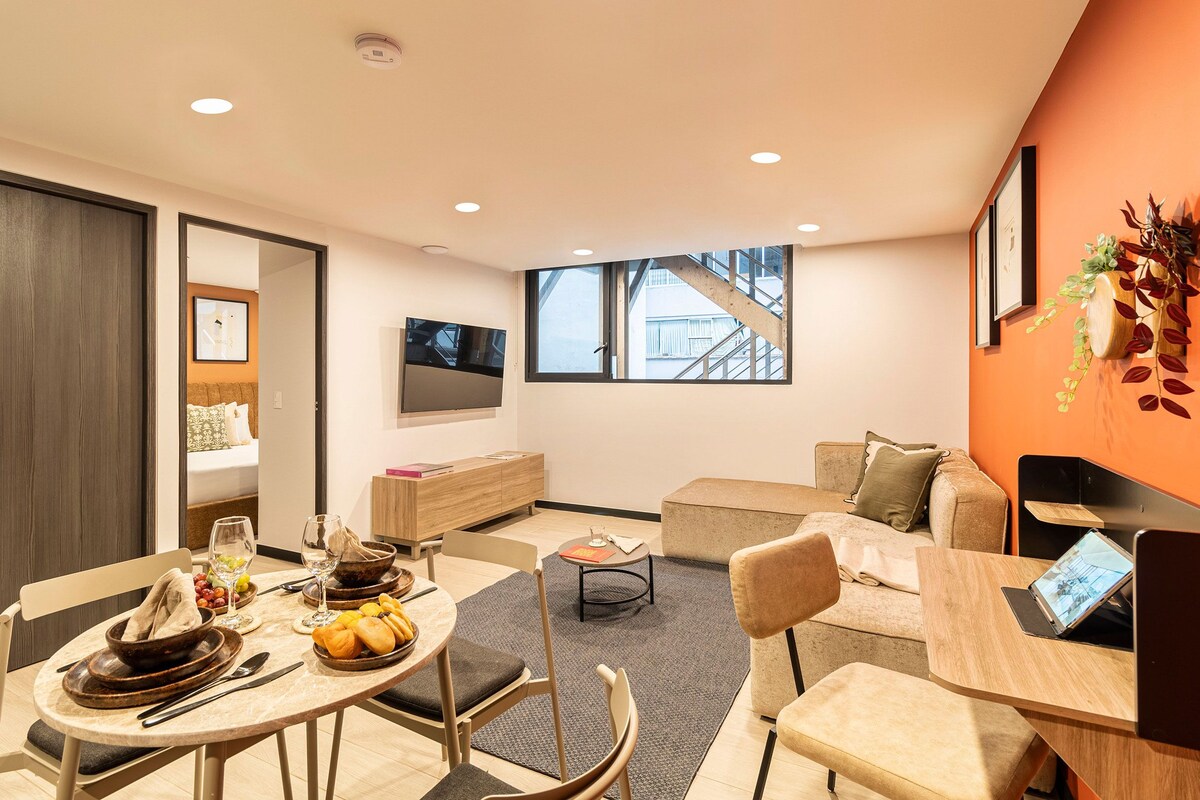 A modern living room with a dining area, a sofa set, a TV, and a staircase leading to an upper floor.