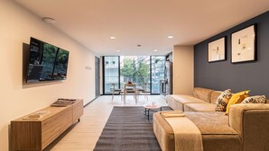 A modern living room with a sofa, a coffee table, a TV mounted on the wall, and a balcony with a view. - Casa Sócrates By Kukun (Mexico City)