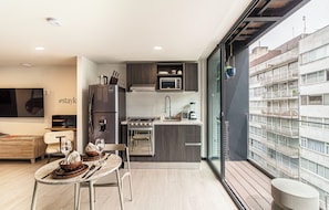 Eine moderne Küche mit Einbauofen, Mikrowelle und Spüle. Es gibt einen Essbereich mit Tisch und Stühlen sowie einen Balkon mit Blick auf die Stadt.
