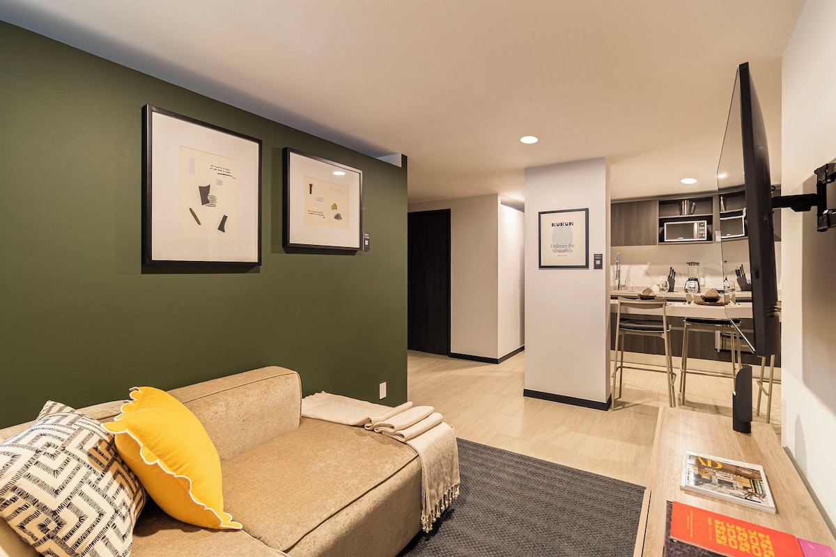 A modern living room with a sofa, a yellow pillow, and framed artwork on the wall.