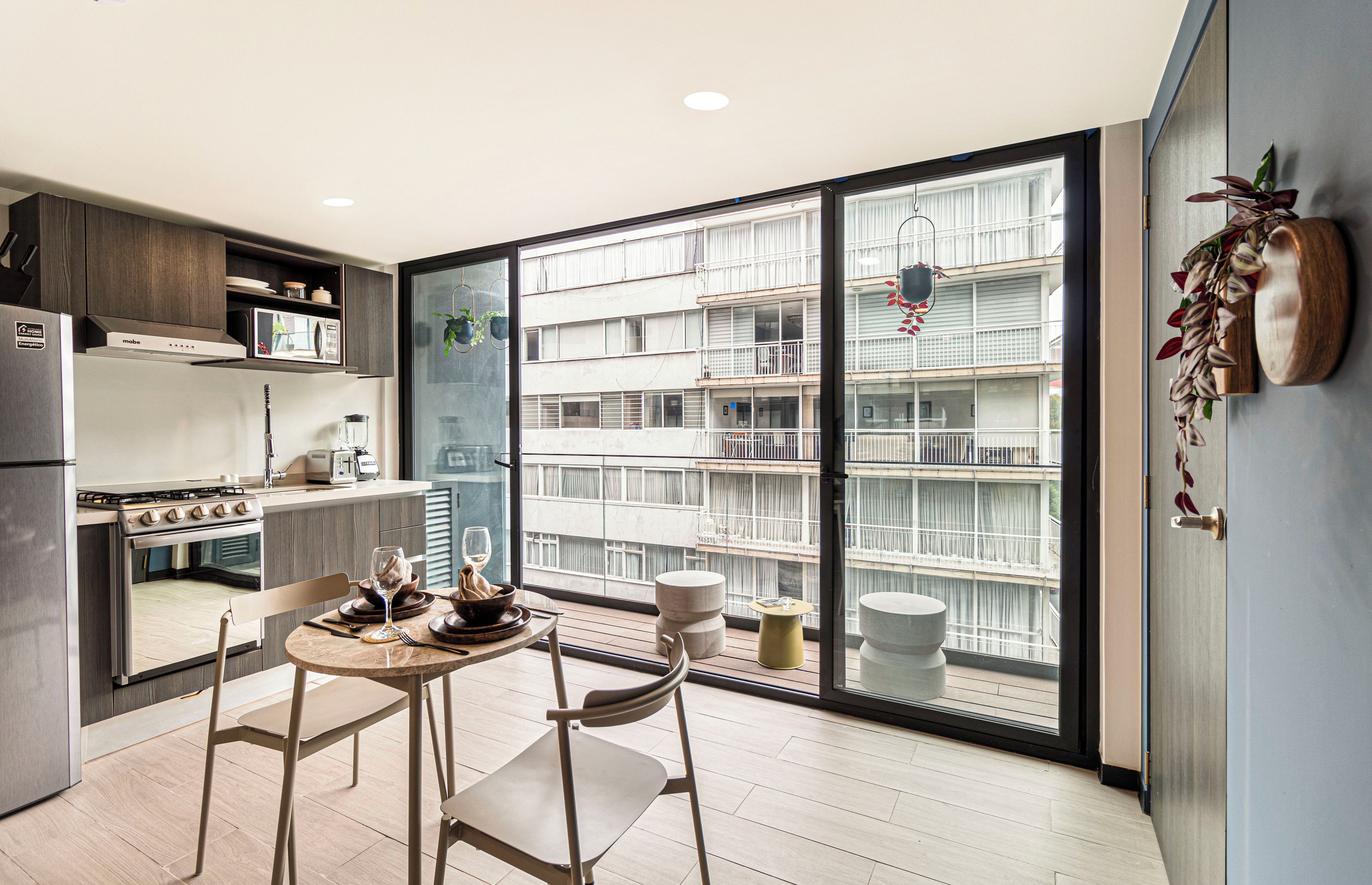 Una cocina moderna con comedor, ventanas amplias y vista a un edificio residencial.
