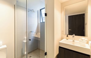 A modern bathroom with a glass-enclosed shower, a white sink with a mirror, and a dark wooden cabinet. - Casa Sócrates By Kukun (Mexico City)
