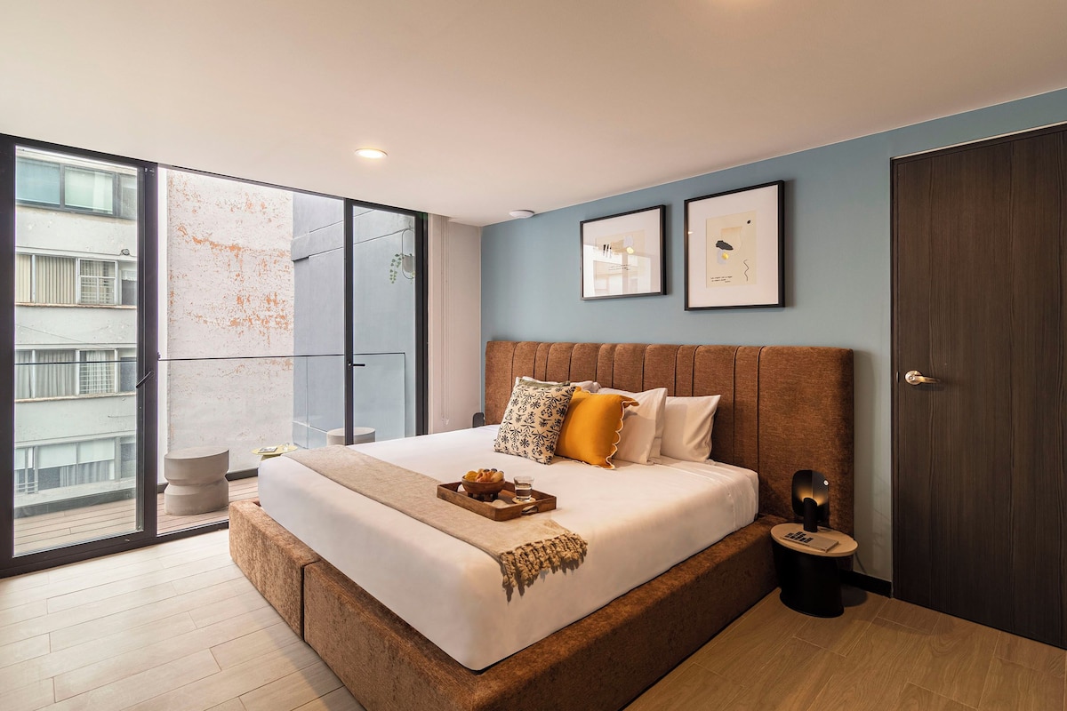 Un dormitorio moderno con una cama grande, una mesita de noche pequeña y vistas al exterior a través de un ventanal corredero.