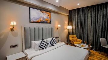 A hotel room with a bed, bedside lamps, a chair, a table with a plate of fruit, and a painting on the wall.
