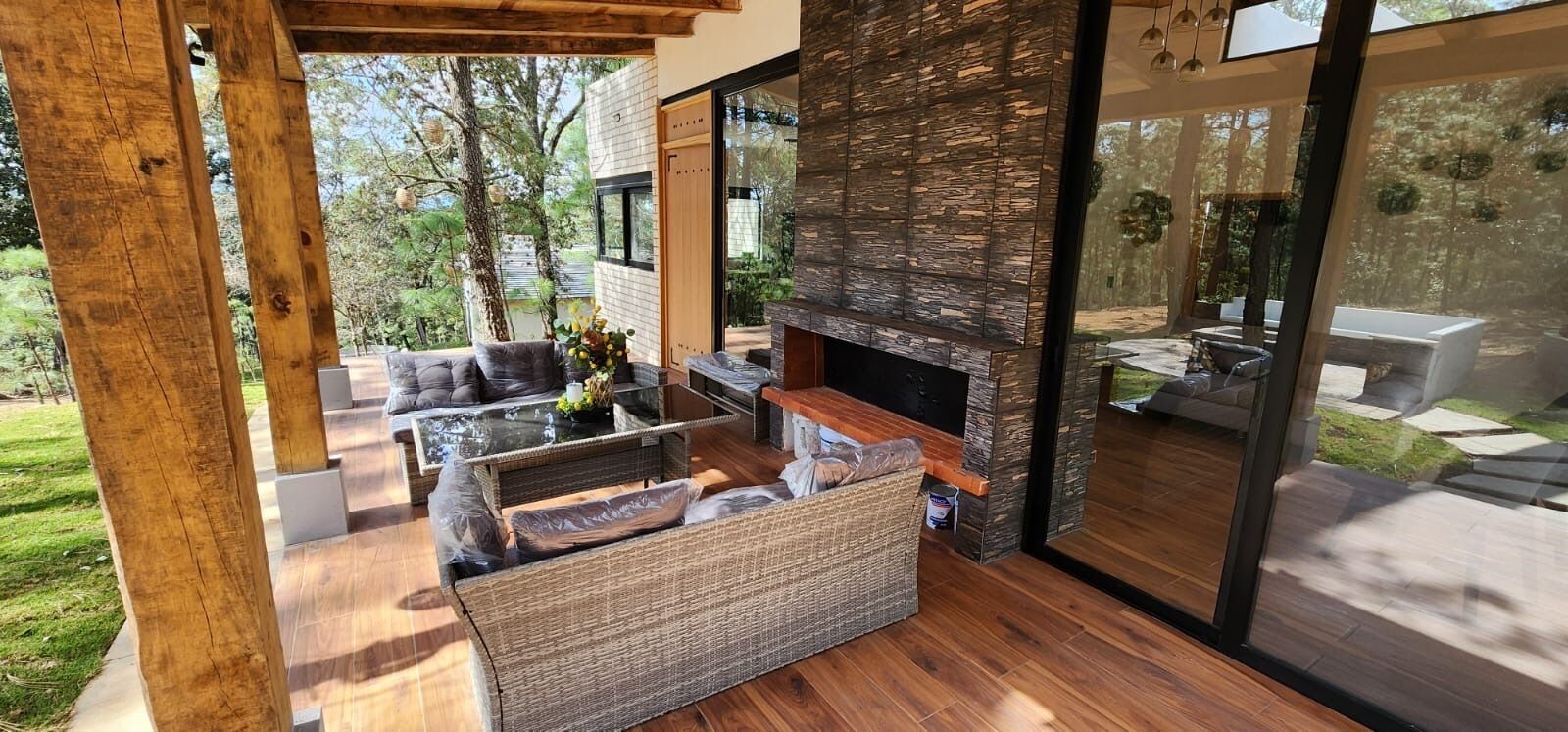 An outdoor living area with a glass enclosure, wicker furniture, and a stone fireplace.