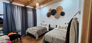 A room with two beds, a small table, and a hanging towel rack.