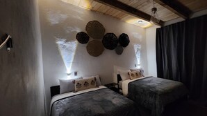 Une chambre avec deux lits, un ventilateur de plafond et des œuvres d’art décoratives au mur.