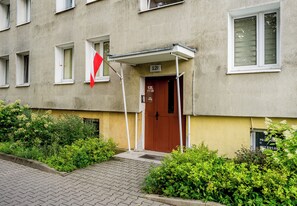 Un edificio con una puerta marrón, un toldo blanco y una bandera roja.