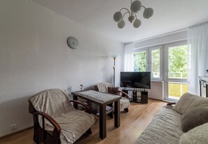A living room with a sofa, chairs, a table, a TV, and a clock on the wall. - Pod Lipami Cozy Apartment (Poznań)