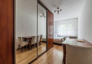 A room with a wooden dining table, chairs, a bed, and a large window with sheer curtains. - Pod Lipami Cozy Apartment (Poznań)