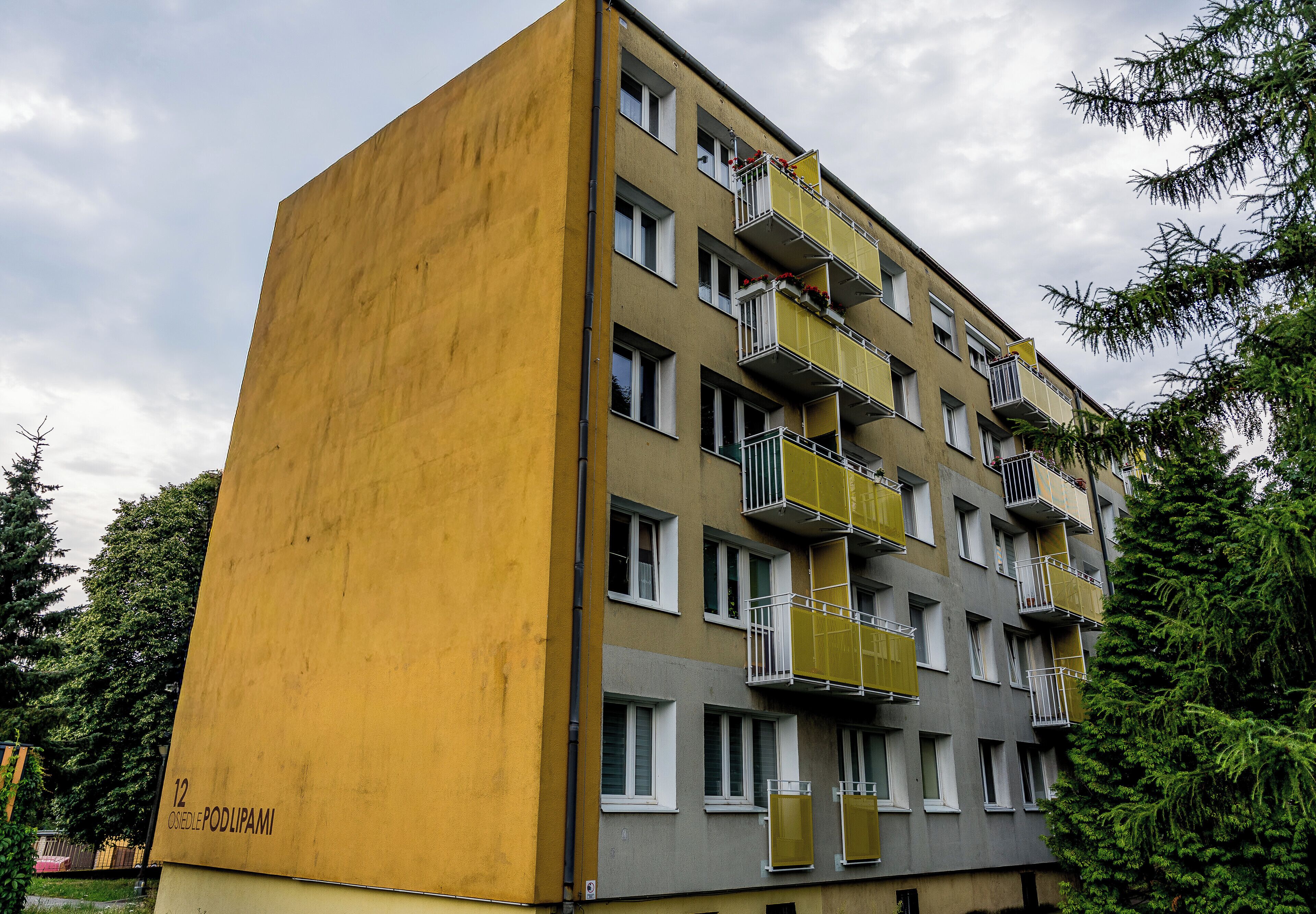 Un edificio de varios pisos con balcones, fachada amarilla y un letrero que indica la dirección.