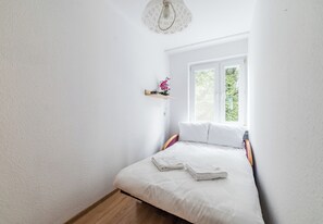 A bedroom with a bed, a window, a shelf with flowers, and a hanging light fixture. - Pod Lipami Cozy Apartment (Poznań)