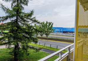 Vista de un árbol verde en primer plano, una vía de tren y un edificio azul con señalización al fondo.