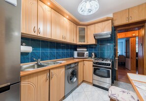 A modern kitchen with wooden cabinets, a stainless steel refrigerator, a washing machine, a microwave, and a stove. - Pod Lipami Cozy Apartment (Poznań)
