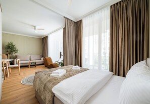 A hotel room with a bed, a sofa, a chair, a small table, and a ceiling fan. - Chmielna Signature Apartment (Warszawa)