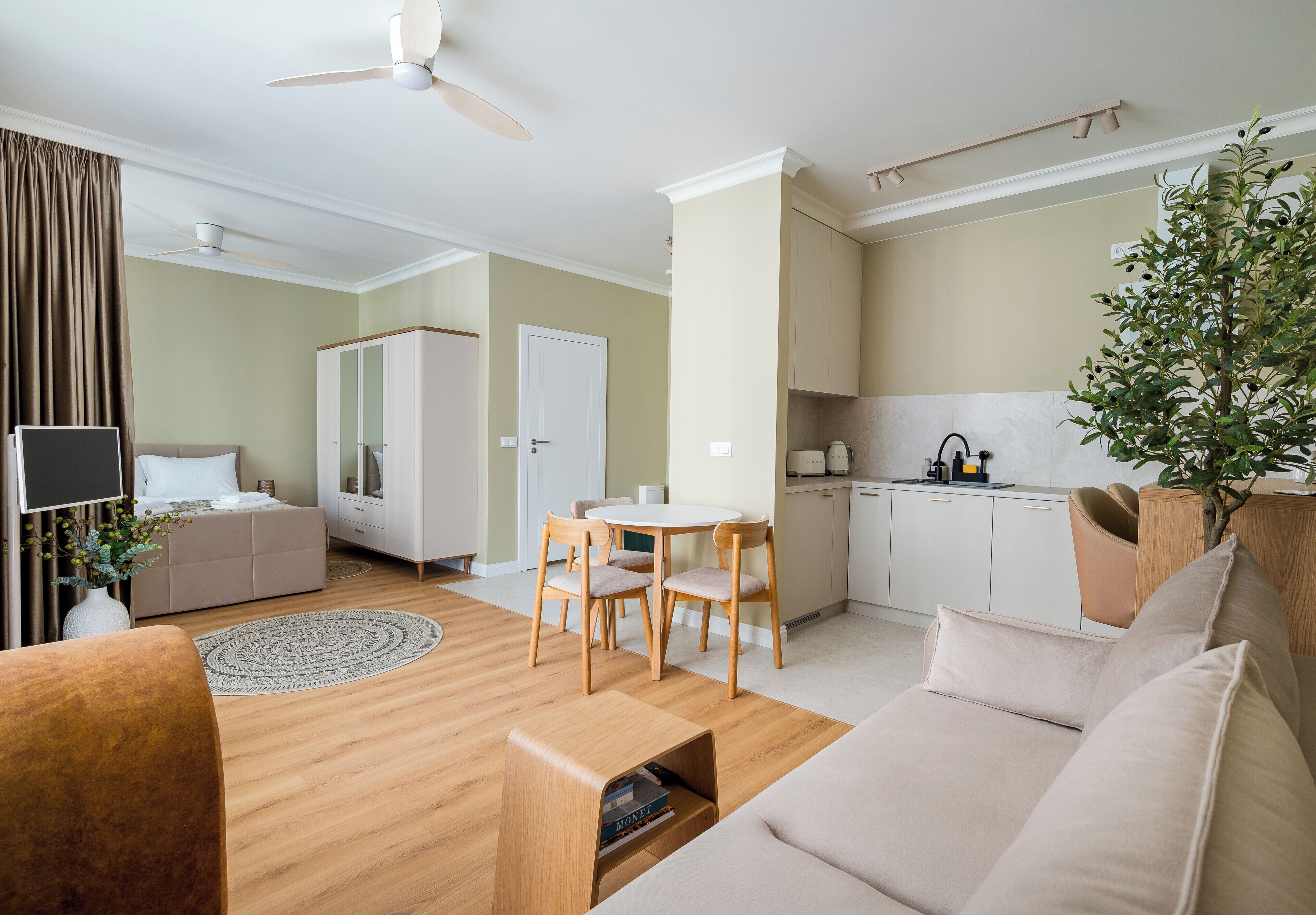 A modern living room with a sofa, a coffee table, and a dining area with chairs. There is a kitchen with cabinets and a sink.