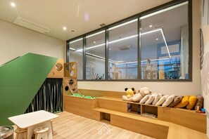 Ein moderner Arbeitsbereich mit großem Fenster, einem grünen Spielbereich und einer Sitzecke mit Kissen.