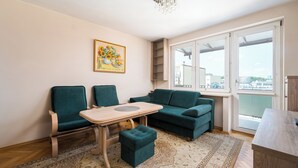 A living room with a sofa, chairs, a small table, a painting, and a view of the city through large windows. - Solec Powiśle Standard Apartment (Warszawa)