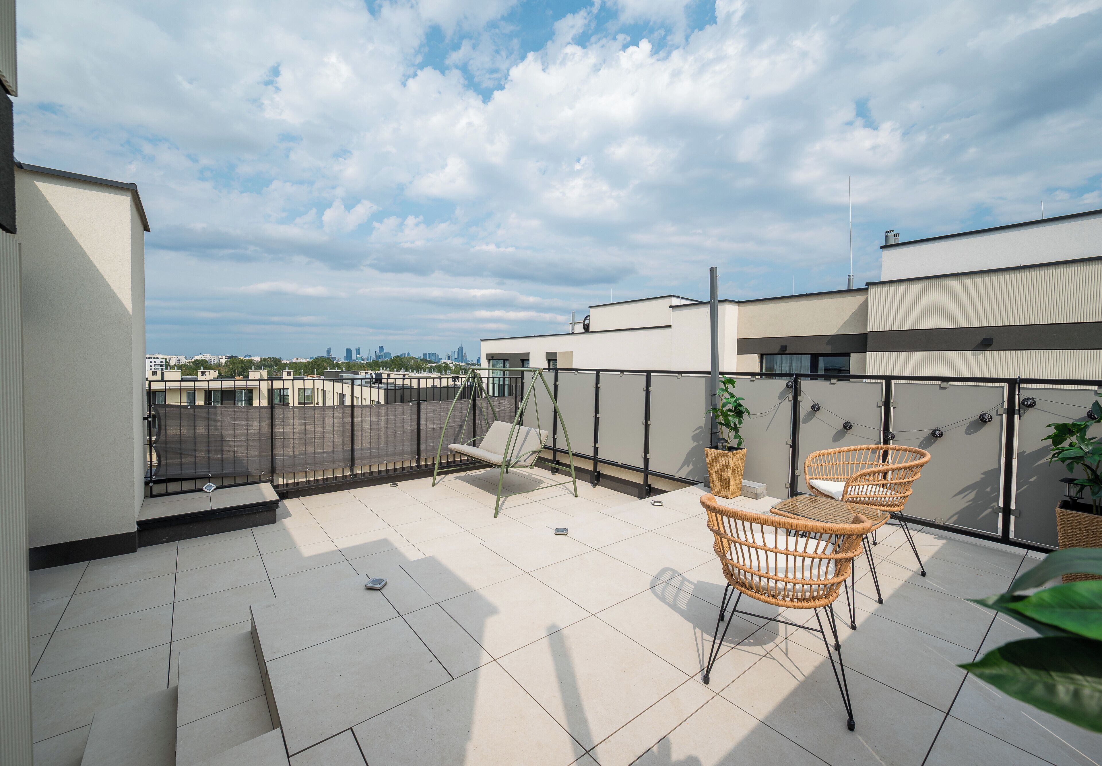 A rooftop terrace with a swing chair, two wicker chairs, and potted plants.