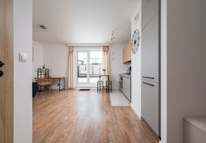 A modern kitchen with a dining area, wooden flooring, and a view through the glass door. - Łopuszańska Modern Studio with Balcony (Warszawa)