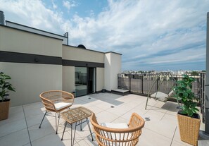 A rooftop terrace with two wicker chairs, a glass door entrance, and a view of the cityscape. - Łopuszańska Modern Studio with Balcony (Warszawa)