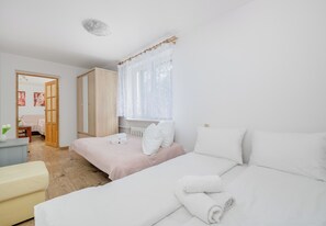 Ett hotellrum med två sängar, en garderob i trä, ett fönster med tunna gardiner och ett litet bord med en vas med blommor.