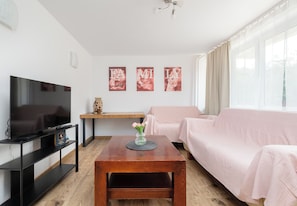 Un salon équipé d’un téléviseur à écran plat, d’une table basse en bois, d’un canapé rose et de trois tableaux encadrés accrochés au mur.