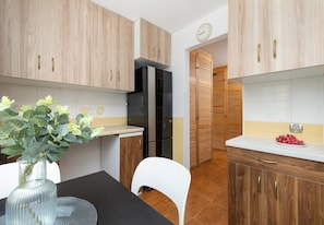 Une cuisine moderne avec des meubles en bois, un réfrigérateur, une chaise blanche et un vase rempli de fleurs.